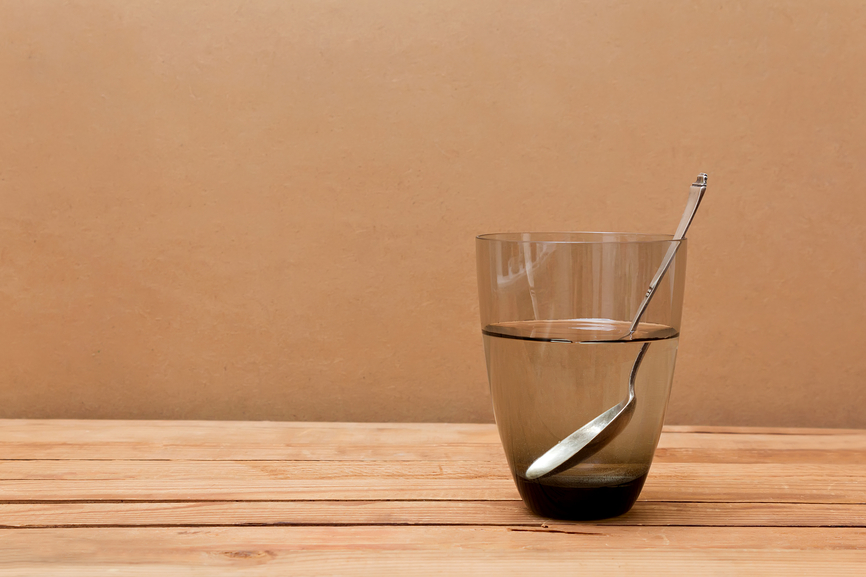 Glass of water and spoon on wooden table.